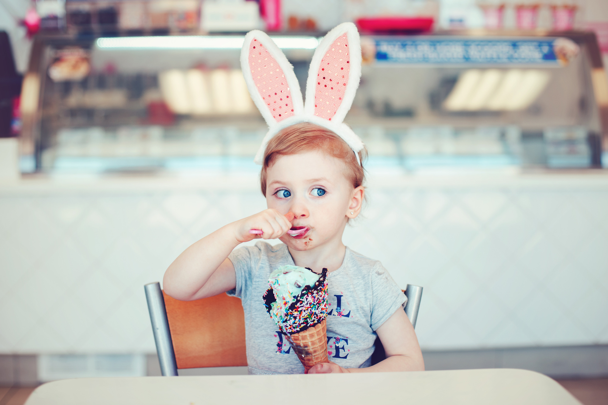 A little girl wearing bunny ears and eating a big ice cream cone with Blue Bell Ice Cream.