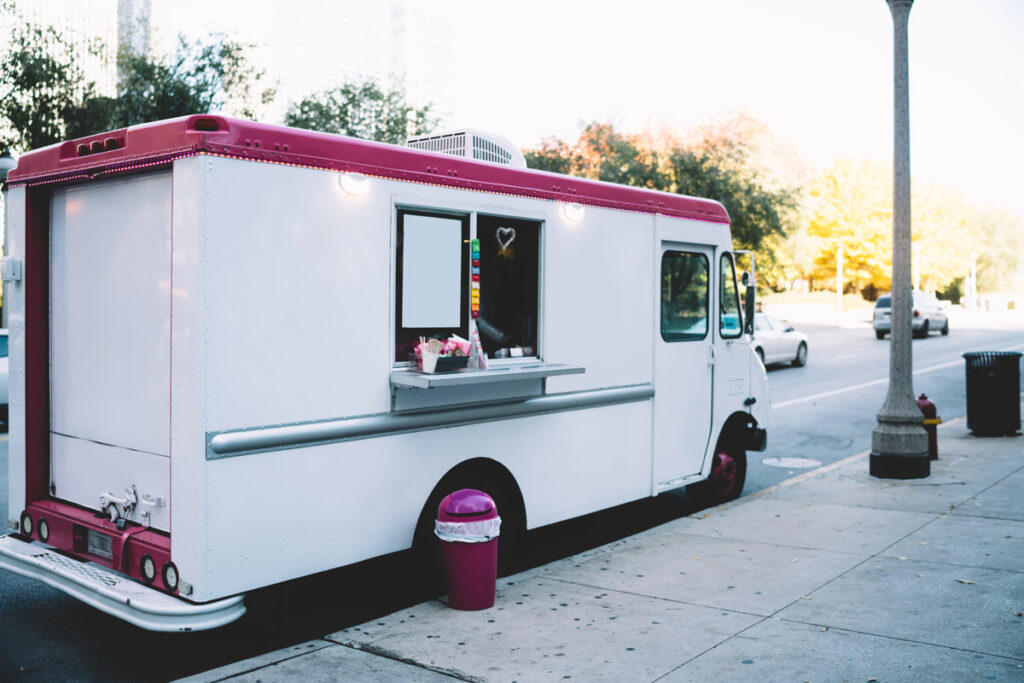 A pink and white ice cream truck parked on the street in Norman.